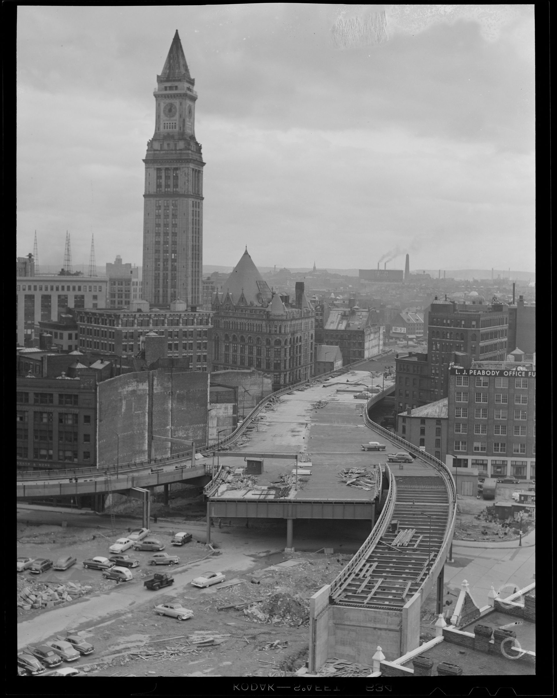 Black and white photograph of ongoing elevated highway construction in front of Customs House Tower